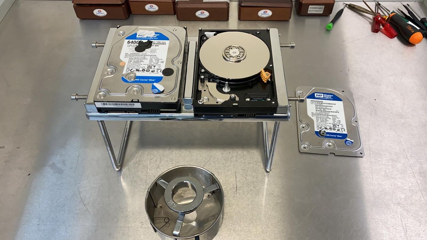 Two hard drives on a metal stand, one with its cover removed to show the platter