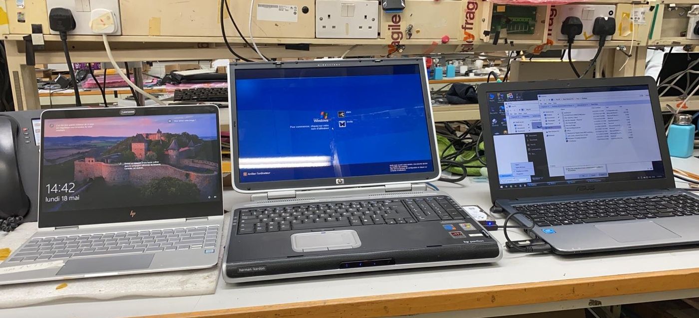 Three laptops switched on and running side by side on a workshop bench