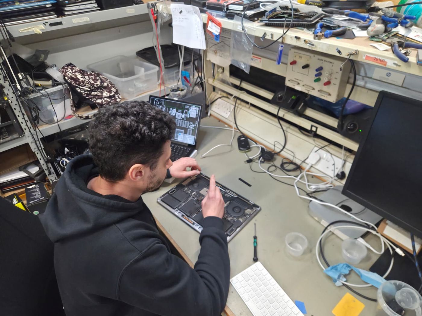 A technician working on an opened laptop with the board schematic on a second screen