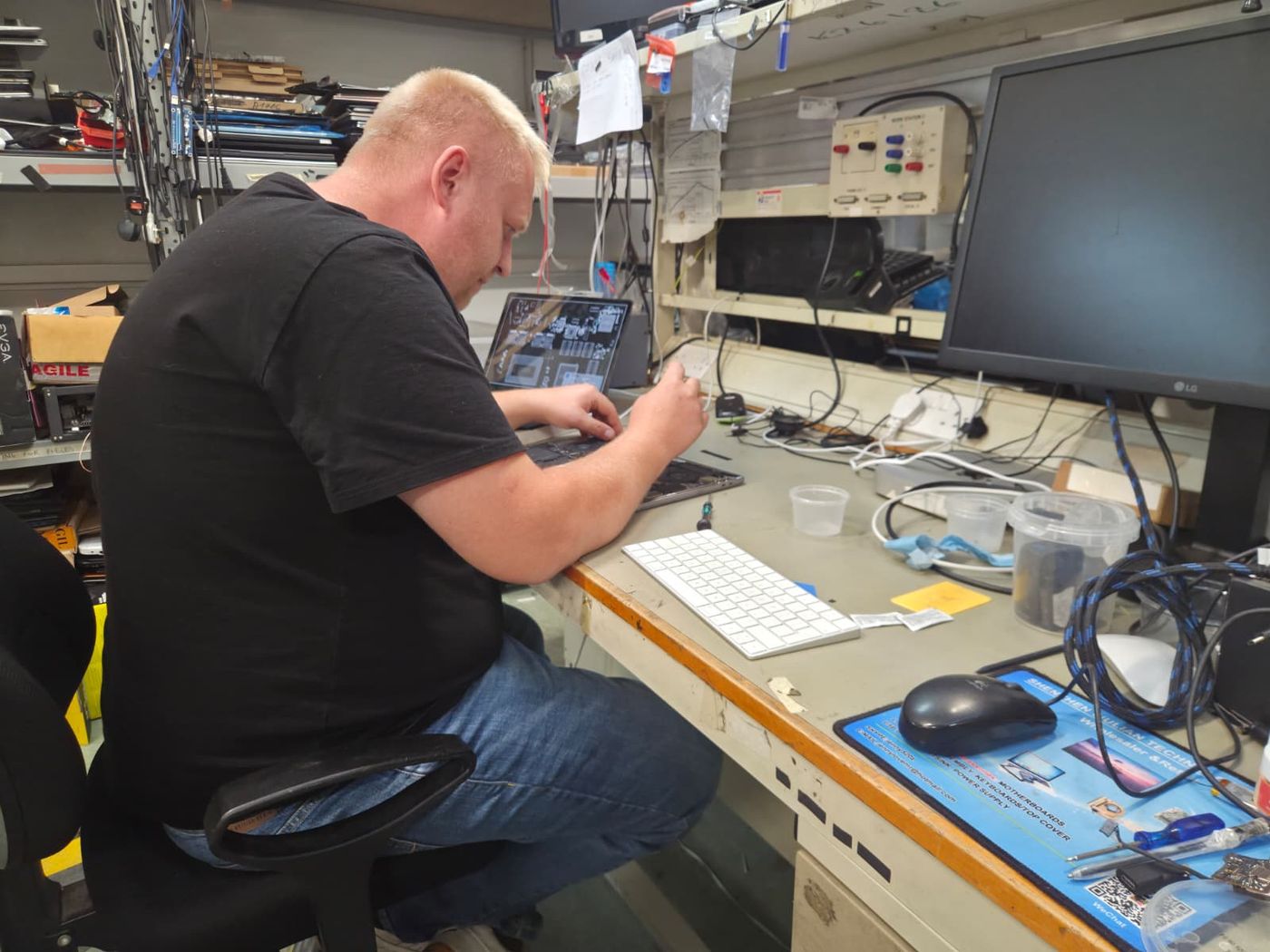 A technician using a screwdriver on an opened laptop at a workshop bench